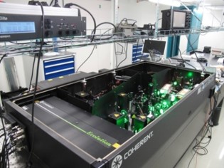 Femtosekundenlaser Lasersystem in einem geöffneten schwarzen Kasten. Man sieht viele optische Element und das grüne Licht des Pumplasers.